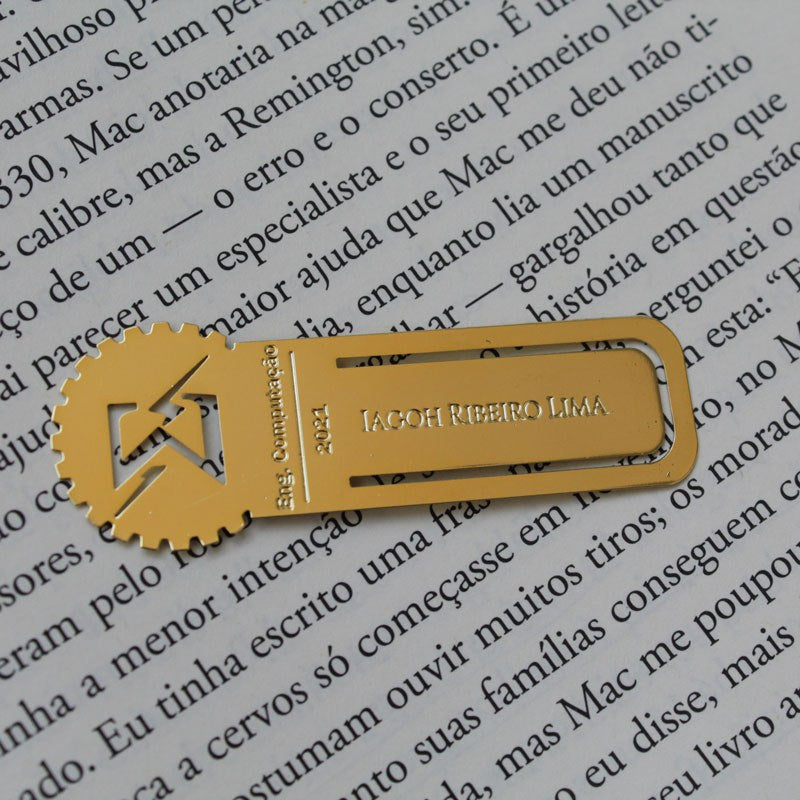 Marcador dourado com símbolo de Engenharia da Computação sobre livro aberto